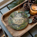 A wooden tray with a decorative ornament featuring a waterfall and a house, along with pine cones and a lit candle, creating a cozy and festive atmosphere.