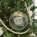 A circular ornament hanging on a Christmas tree, featuring a tropical landscape with palm trees and a body of water.