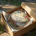 A round ornament in a box, featuring a scenic landscape of Waimea Canyon State Park, Hawaii.