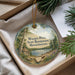 A round ornament with a scenic image of Walden Pond, a state reserve in Massachusetts, is displayed in a box with pine branches.