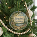 A round ornament on a Christmas tree, featuring a scenic landscape with a lake and a cabin, surrounded by pine trees and beaded ornaments.