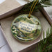 A decorative ornament in a box, featuring a scenic image of Warren Woods State Park, Michigan.