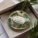 A decorative ornament with a scenic landscape of the Warwick State Forest in Massachusetts, featuring a waterfall, pine trees, and a sign indicating a "National Park".