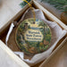 A circular ornament with a scenic forest landscape, featuring a waterfall, pine trees, and a sign indicating the Warwick State Forest in Massachusetts.