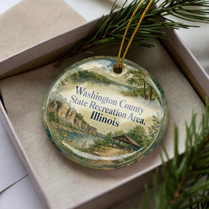 A decorative ornament in a box, featuring a scenic landscape with a river, trees, and a building.