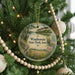 A round ornament on a Christmas tree, featuring a scenic landscape with a bird, surrounded by ornaments and lights.