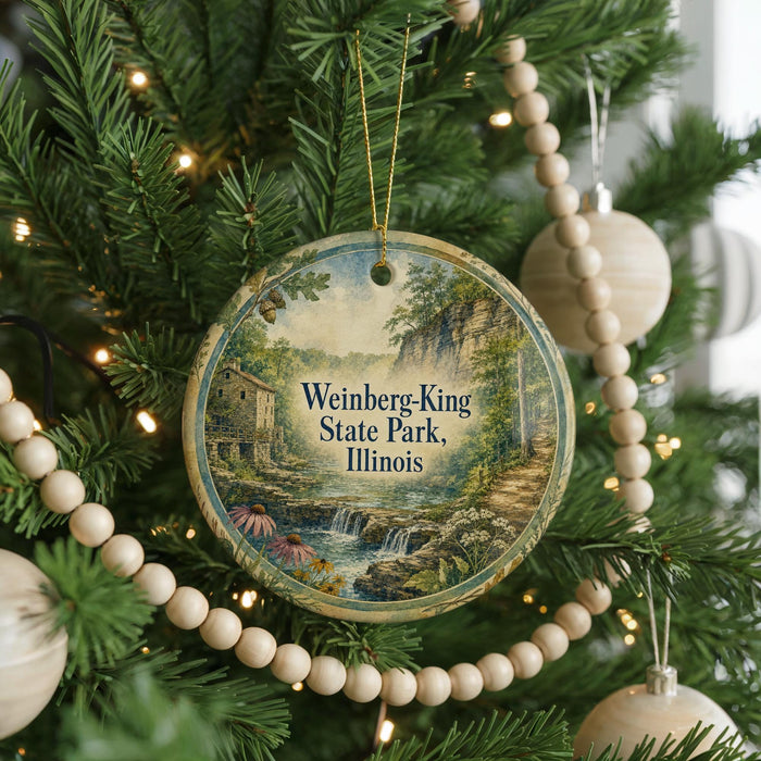 A round ornament hanging on a Christmas tree, featuring a scenic landscape with a waterfall and a house.
