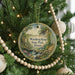 A round ornament hanging on a Christmas tree, featuring a scenic landscape with a waterfall and a house.