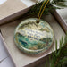 A decorative ornament in a box, featuring a scenic image of the Wekiva Springs State Park in Florida.