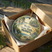A circular ornament in a wooden box, featuring a scenic landscape with a bird and a waterfall, with the text "Wells State Park, Michigan" printed on it.