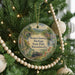 A Christmas tree ornament with a scenic image of a train and a bridge, surrounded by greenery and lights.