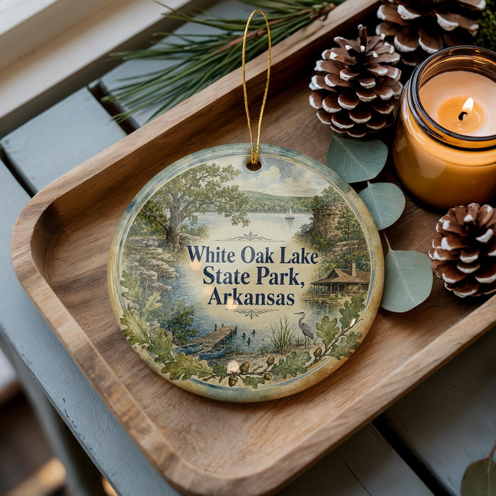 A decorative ornament with a scenic image of White Oak Lake State Park, Arkansas, is displayed on a wooden tray alongside pine cones and a lit candle.