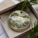 A decorative ornament in a box, featuring a scenic image of Wild River State Park in Minnesota.