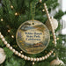 A round ornament hanging on a Christmas tree, featuring a scenic landscape with a house and trees.