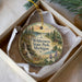 A decorative ornament in a box, featuring a scenic landscape with a waterfall, pine trees, and a deer.