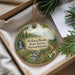 A round ornament with a forest scene and a path, hanging from a string.