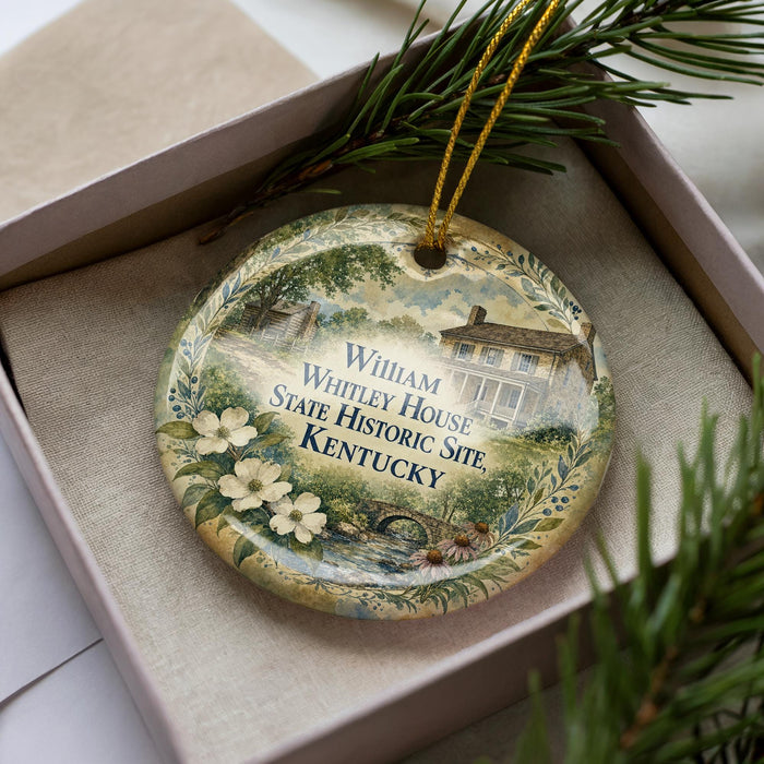 A decorative ornament in a box, featuring a painting of a house surrounded by flowers and greenery, with the text "William Whitley House State Historic Site, Kentucky" on it.