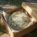 A decorative ornament in a wooden box, featuring a house and flowers, with the text "William Whitley House State Historic Site Kentucky" printed on it.