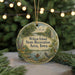 A round ornament with a scenic landscape and text, hanging on a string.