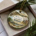 A decorative ornament with a scenic landscape of Wilson State Park, Kansas, displayed in a box with pine branches.
