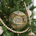 A round ornament hanging on a Christmas tree, featuring a scenic landscape with a waterfall and a cabin.