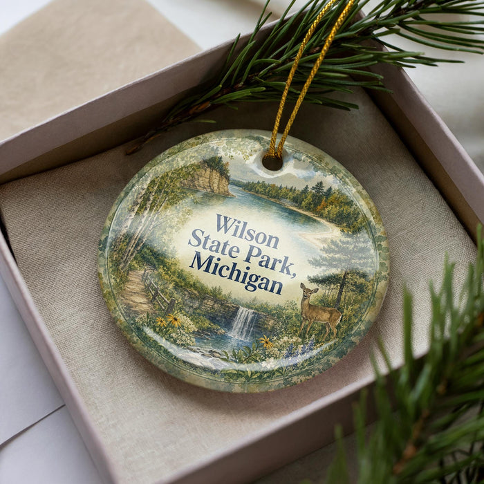 A decorative ornament in a box, featuring a scenic landscape with a waterfall, pine trees, and a deer.