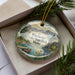 A decorative ornament featuring a scenic landscape of Winchester Lake State Park in Idaho, with a boat on the lake and mountains in the background.