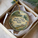 A round ornament in a box, featuring a scenic image of a park with a lake and trees, along with the text "Wolfe's Neck Woods State Park, Maine".