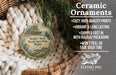 Ceramic ornaments, featuring a round ornament with a scenic landscape and text, are displayed in a basket with pine branches.