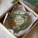 A decorative ornament in a box, featuring a scenic landscape with a waterfall, a house, and flowers.