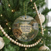 A round ornament hanging on a Christmas tree, featuring a scenic landscape with a waterfall and a house.