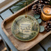 A wooden tray with a decorative ornament featuring a scenic image of Wormsleeve Historic Site, State Park, Georgia, and a candle on a table.