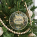A circular ornament hanging on a Christmas tree, featuring a scenic landscape with pine trees, a river, and a sign that reads "Wrentham State Forest, Massachusetts".