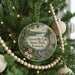 A round ornament hanging on a Christmas tree, featuring a scenic landscape with a lake and a waterfall.