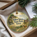 A decorative ornament with a scenic image of a park, featuring a deer and a cabin, is displayed in a box with pine branches.