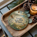 A decorative ornament with a scenic image of Young State Park, Michigan, featuring a bird, pine cones, and a candle on a wooden tray.