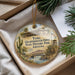 A decorative ornament with a picture of a historical building and a cactus, placed in a box with pine branches.