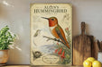 A framed illustration of a hummingbird, titled "Allen's Hummingbird", is displayed on a shelf next to a wooden cutting board and a potted plant.