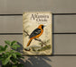 a metal sign with an illustration of an orange and black bird, likely an oriole, perched on a branch.