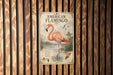 a vintage-style metal sign with an illustration of an American flamingo, mounted on a wooden wall.