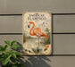 a vintage-style metal sign depicting an American flamingo, with a lush green plant in the foreground.