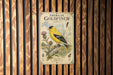 A vintage-style metal sign depicting an American Goldfinch, with illustrations of the bird and its natural habitat.