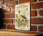 A vintage-style metal sign featuring an illustration of a yellow finch, with text describing the bird and its habitat.