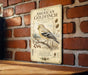A vintage-style metal sign featuring an illustration of a golden finch perched on a branch, with text describing the bird and its habitat.
