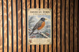 A vintage-style metal sign with an illustration of a robin in winter snow, mounted on a wooden wall.
