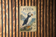 A vintage-style metal sign with an illustration of a puffin bird, placed on a wooden wall.