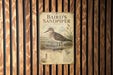 A vintage-style metal plaque with a detailed illustration of a sandpiper bird, mounted on a wooden wall.