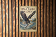 A vintage-style poster of a bald eagle with salmon in its talons, displayed on a wooden wall.