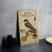 a vintage-style sign with illustrations and text about a Bank Swallow, placed on a table next to some black camera lenses.