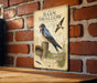 a vintage-style metal sign with illustrations of two blue birds, likely barn swallow birds, perched on a wooden post against a brick wall.